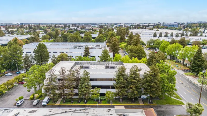 Aerial view of 3235 Kifer Rd, a three-story office building among trees, with Santa Clara's business parks behind it